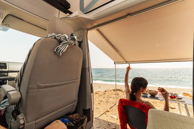 Rear view of woman eating food while sitting at beach