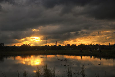 Scenic view of lake against dramatic sky during sunset