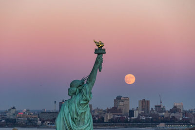 Statue of liberty in city during sunset