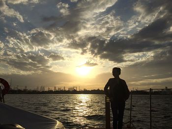 Rear view of man standing by sea against sky during sunset