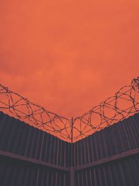 Low angle view of barbed wire on fence against orange sky