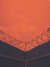 Low angle view of barbed wire against orange sky