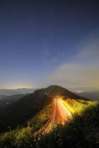 Illuminated road amidst landscape against sky at night
