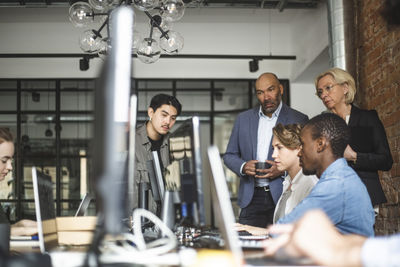 Male and female hackers explaining investors over computer at creative office