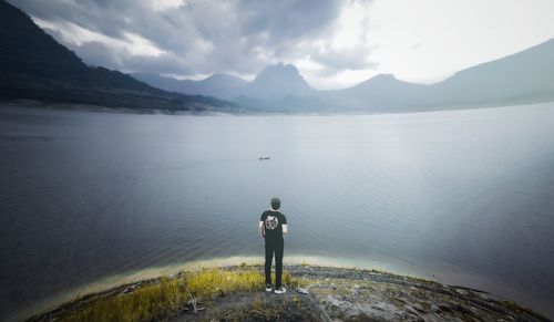 Rear view of man standing by lake against mountains