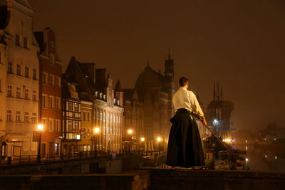 Rear view of man practicing martial arts while standing on retaining wall in city during sunset