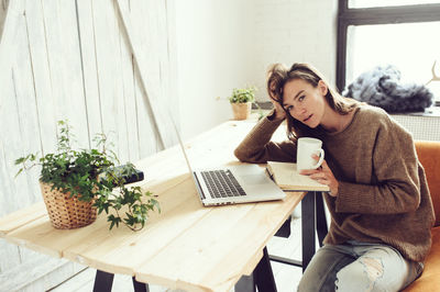 Portrait of woman having drink with laptop at table