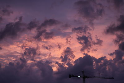 Low angle view of silhouette cranes against dramatic sky