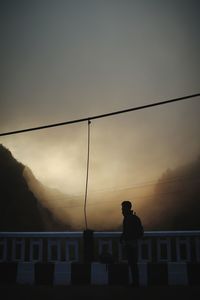 Silhouette men standing on railing against sky during sunset