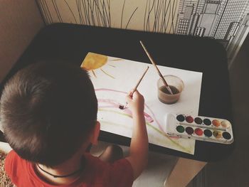 High angle view of boy painting on paper at table