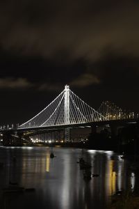 Illuminated bridge over river against sky at night