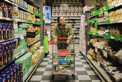 Female customer with shopping cart on alley at supermarket