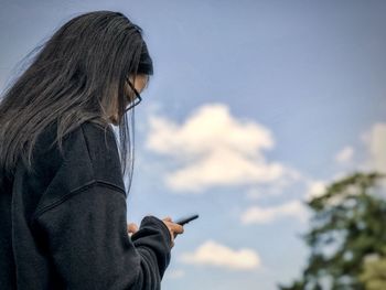 Woman holding smart phone against sky