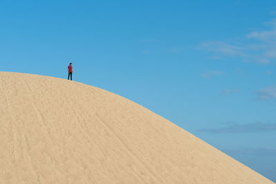 Low angle view of man standing on sand dune against blue sky