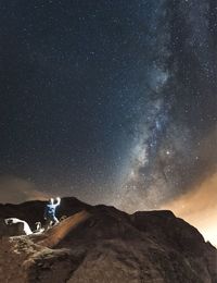 Man with illuminated lighting equipment on mountain against milky way