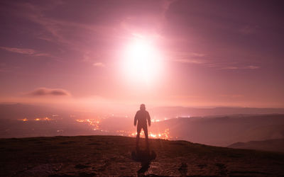 Rear view of silhouette man standing on mountain against sky during sunset