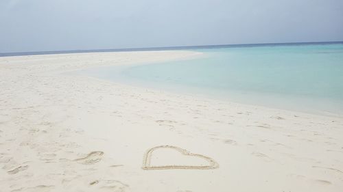 Heart shape on sand at beach against sky