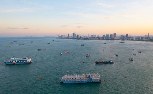 Boats in sea by buildings against sky during sunset