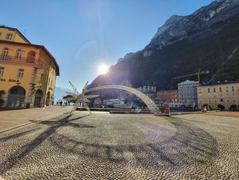 Road by buildings against sky on sunny day