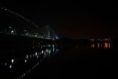 Illuminated bridge over river in city at night