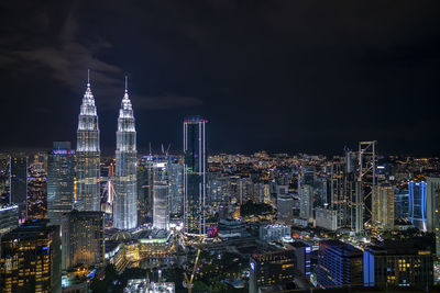 Illuminated modern buildings in city against sky at night