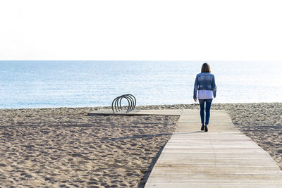 Rear view of a woman walking on footpath to seashore in sunny day