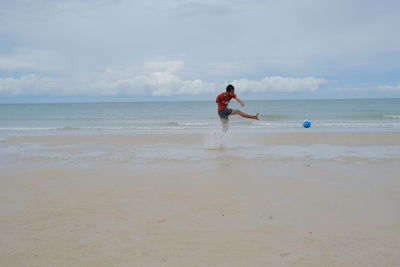 Man playing with ball on beach against sky
