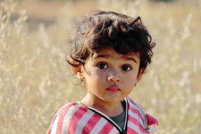 A small boy of indian origin stands in the garden looking at the camera. 