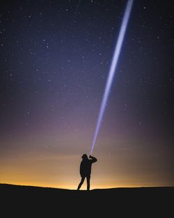 Silhouette man with illuminated flashlight against star field
