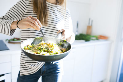 Young woman holding pan with vegan pasta dish