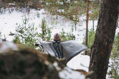 Young brunette beautiful woman in hat and grey poncho walking in the winter forest