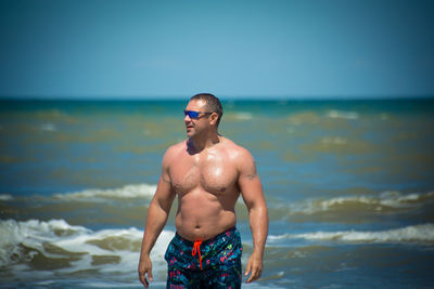 Shirtless man standing at beach against clear sky