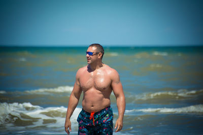 Full length of shirtless man standing at beach against sky