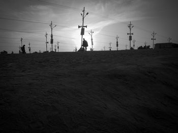 Silhouette electricity pylon on field against sky during sunset