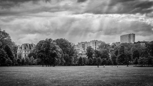 Trees and cityscape against cloudy sky