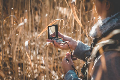 Side view of woman holding navigational compass while standing amidst plants