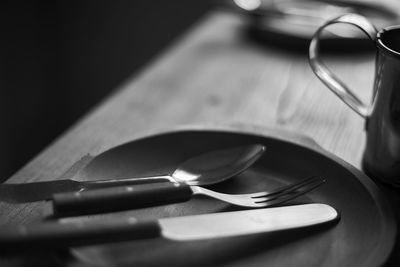 Trio. spoon, fork and knife in the wooden plate. defocused black and white background. close up.