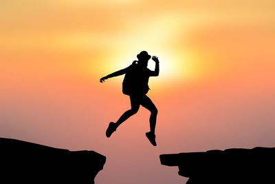 Silhouette person jumping over rocks against sky during sunset