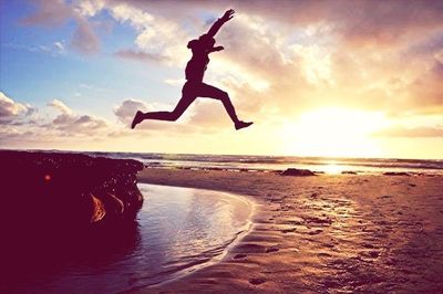 Silhouette of woman jumping on beach at sunset