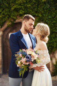Romantic newlywed couple with bouquet standing outdoors