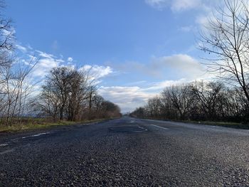 Empty road amidst bare trees against sky