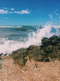 Scenic view of sea waves splashing on shore against sky