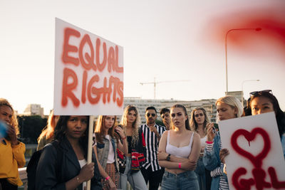 Women and men with posters protesting for equal rights against sky in city