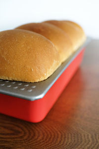 Close-up of homemade bread loaf in baking tray on wooden table against white background