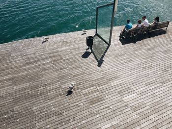 High angle view of people sitting on bench at promenade by sea