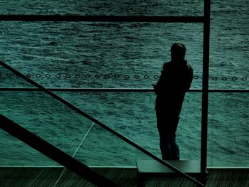 Man standing by glass window in front of sea