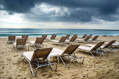 Empty chairs on beach against sky