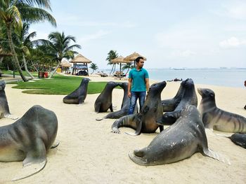 Man standing amidst sea lion statues on shore at beach against sky