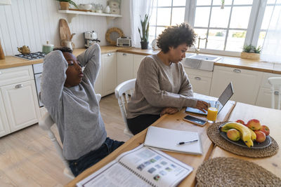 Young freelancer working on laptop with son relaxing at table