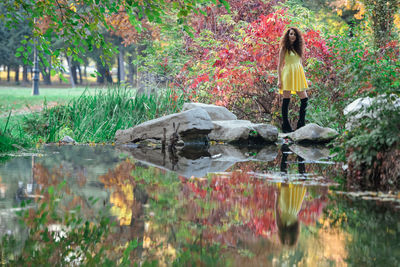 Woman standing by lake with trees in park